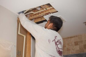 Plumber installing pipe into a wall where sheetrock has been cut for access